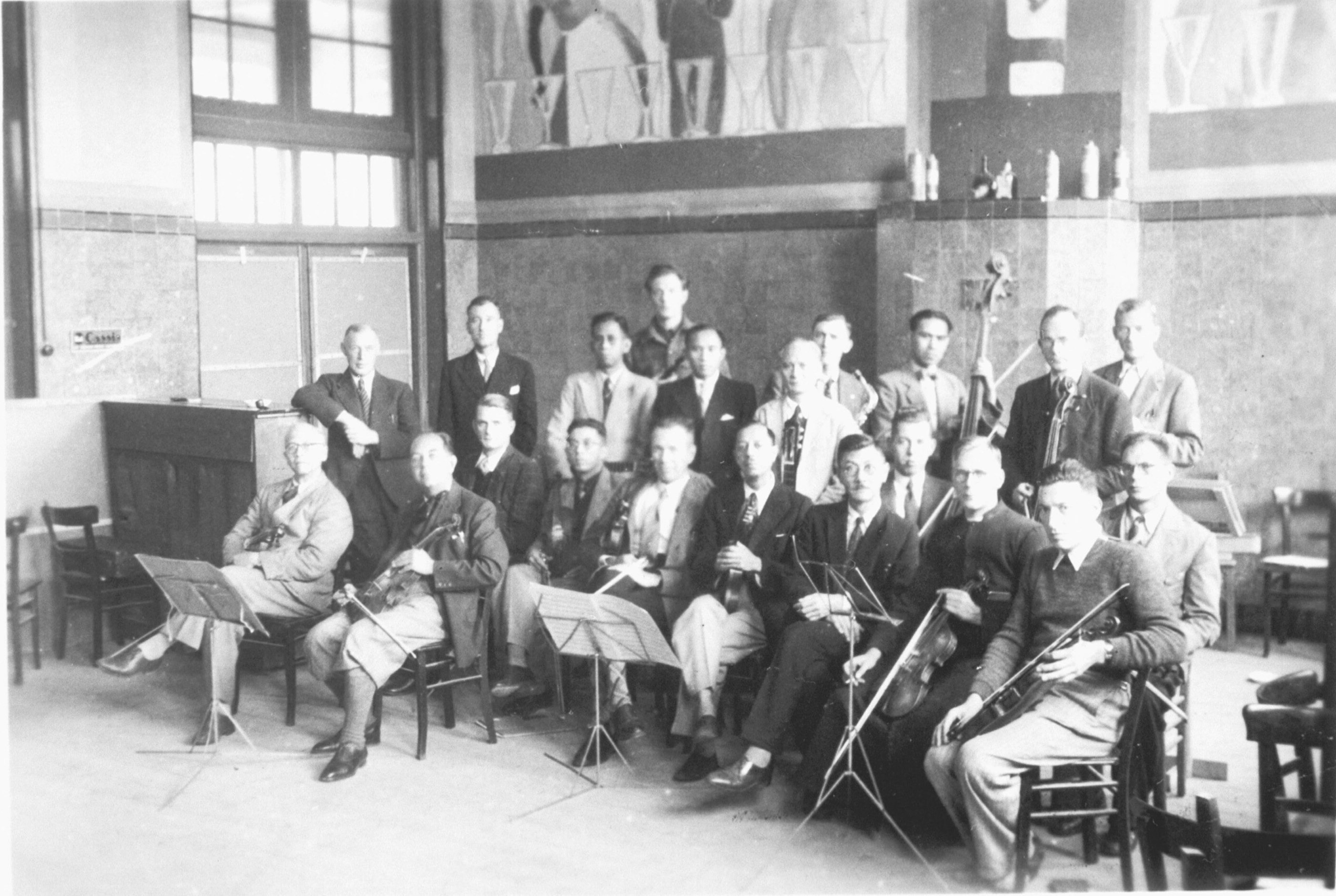 Foto van het Indisch orkest tijdens een repetitie in Kamp Sint-Michielsgestel. Er zijn instrumenten te zien zoals de ukelele, gitaar en viool die vaak in Indische muziekgenres worden gebruikt.