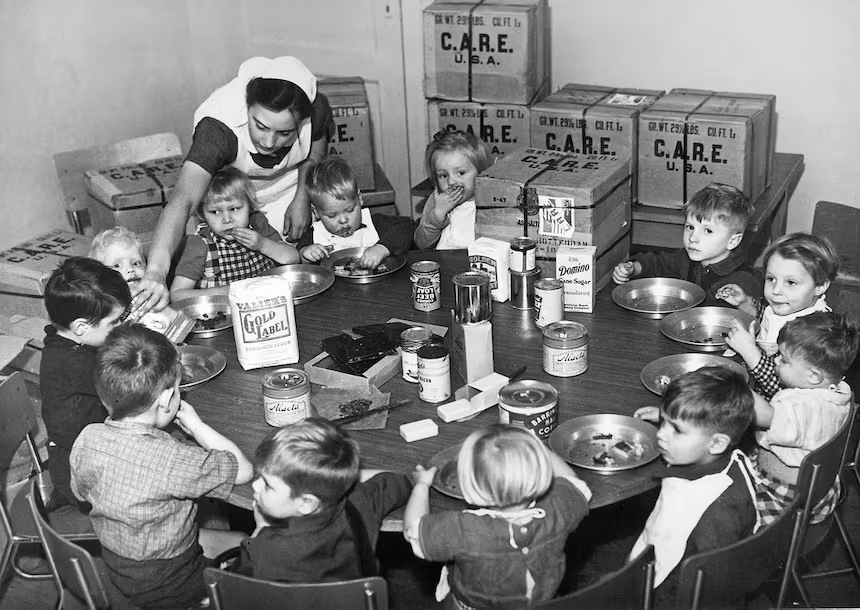 Een verpleegster voedt Nederlandse weeskinderen met levensmiddelen uit CARE-pakketten, circa 1953.  