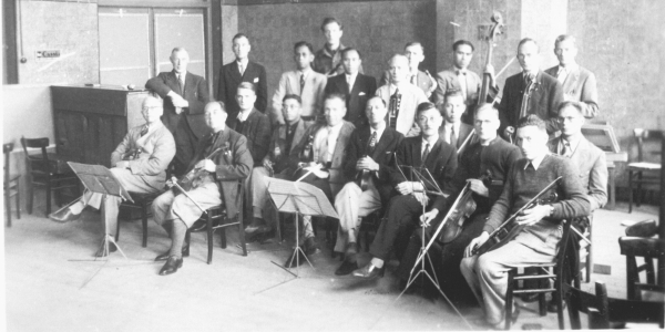 Foto van het Indisch orkest tijdens een repetitie in Kamp Sint-Michielsgestel. Er zijn instrumenten te zien zoals de ukelele, gitaar en viool die vaak in Indische muziekgenres worden gebruikt.