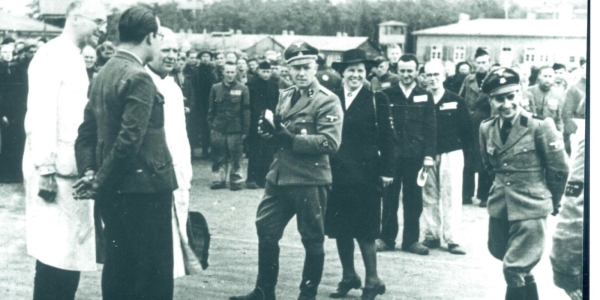 Foto van opnames van een propagandafilm in Kamp Amersfoort. Van links naar rechts: medegevangene en hulparts Jan Tückermann, kampoudste Franciscus H. M. "Frans" van de Laar, medegevangene en hulparts Bernardus Josephus Quirinus van Tilburg, Kampkommandant Karl Peter Berg, Loes van Overeem. De man rechts in uniform rechts was verantwoordelijk voor propaganda maar zijn naam is niet bekend.