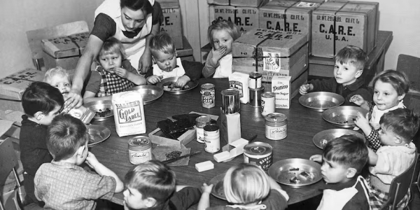 Een verpleegster voedt Nederlandse weeskinderen met levensmiddelen uit CARE-pakketten, circa 1953.  